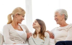 three generations sitting together on a sofa, grandmother, mother, and daughter, 5 Financial Wellness Tips for the Sandwich Generation